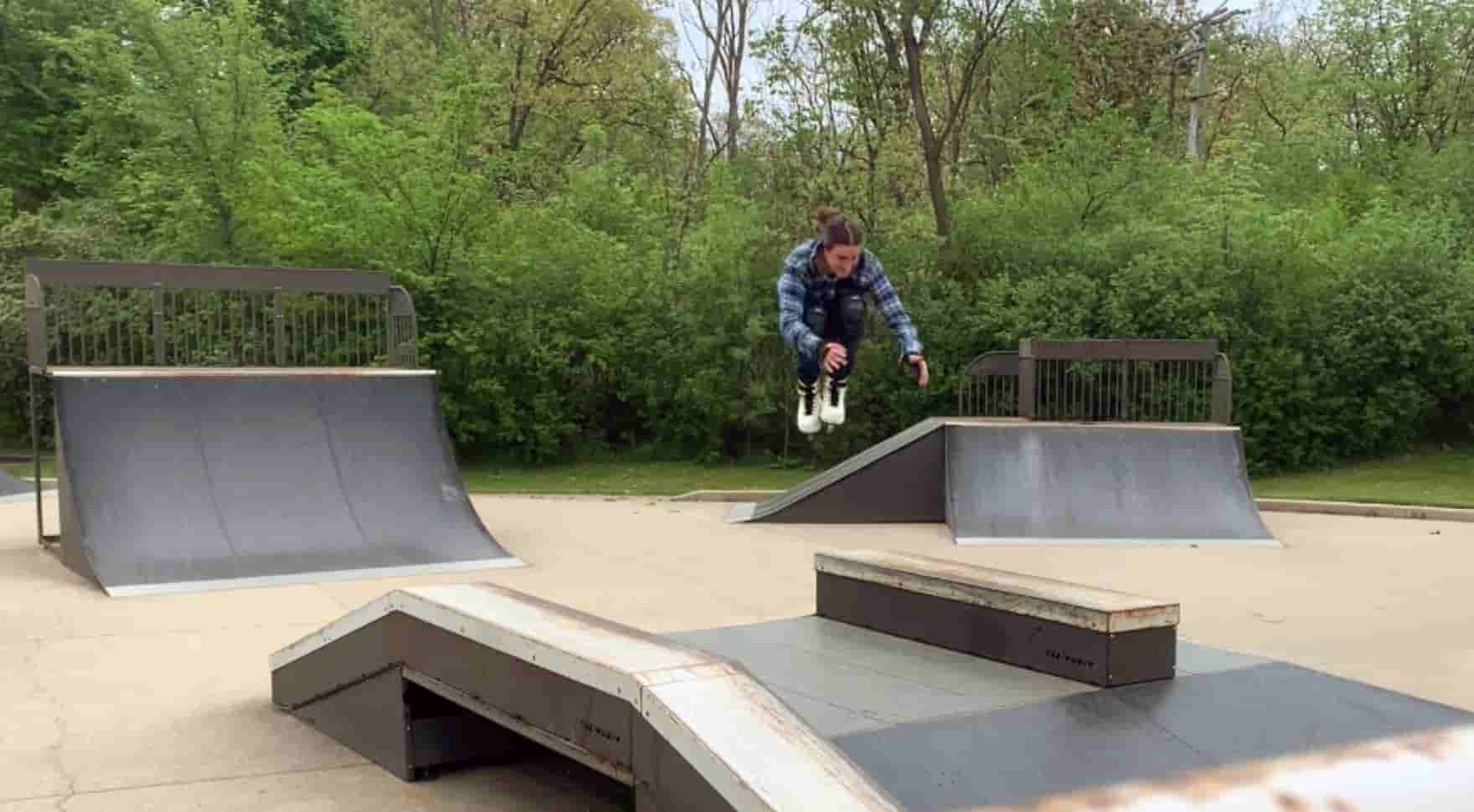 man wearing rolling blades, flying through the air in the tucked position amid ramps and ledges in a wooded area